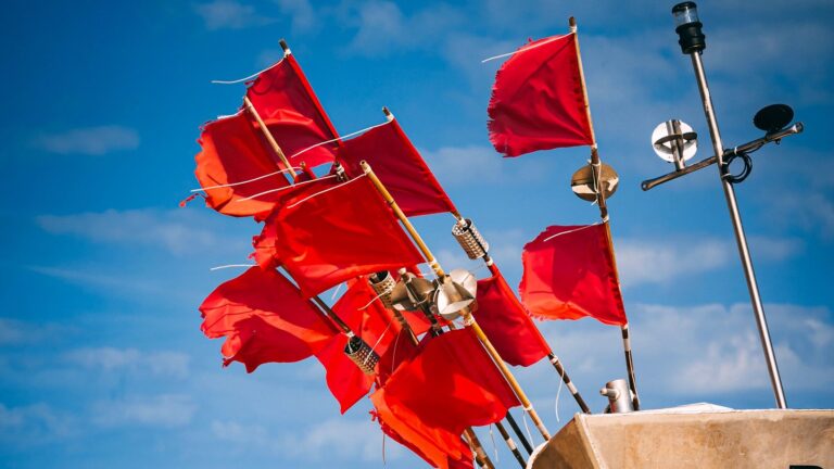 Cluster of red flags on a boat mast, symbolizing Upwork red flags freelancers should watch for before bidding